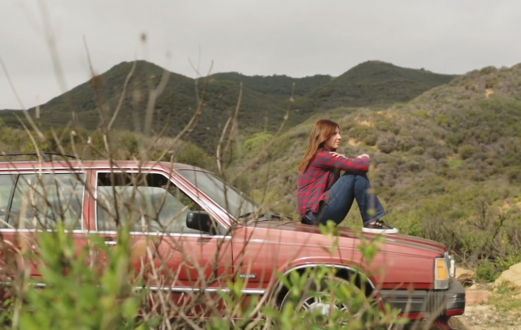 Frau sitzt auf Motorhaube in Landschaft, gedankenverlorenen Blick in Ferne als Titelbild für Zeugnis Dem Vergewaltiger vergeben?