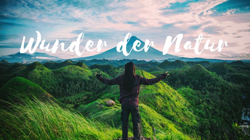 Frau in Berglandschaft breitet Hände aus als Blogbild für Wunder der Natur